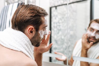 Çekici, genç, üstsüz adam yüz kremi sürüyor.