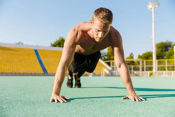 Imagen del hombre concentrado haciendo flexiones en el campo de deportes al aire libre — Foto de Stock