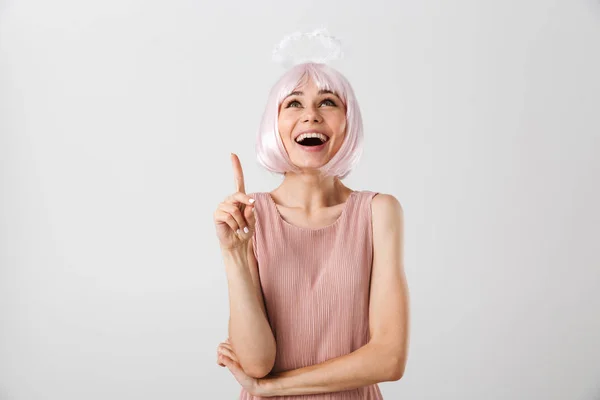 Portret van een lachende opgewonden vrouw met een roze pruik en een halo die naar boven kijkt en met de vinger wijst naar de copyspace — Stockfoto