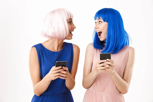 Portré két eksztatikus nőről, akik kék és rózsaszín parókát viselnek, miközben egymásra néznek, miközben mobilon gépelnek. — Stock Fotó