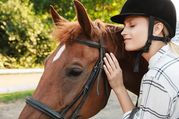 Εικόνα καυκάσιας γυναίκας που φοράει καπέλο και στέκεται δίπλα σε άλογο στην αυλή — Φωτογραφία Αρχείου
