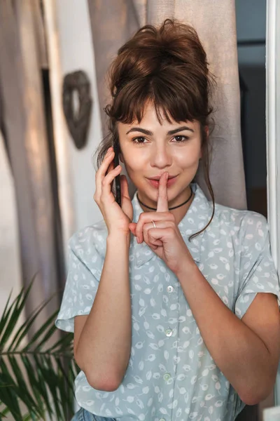 Mooie vrouw praten door mobiele telefoon binnen thuis tonen stilte gebaar. — Stockfoto