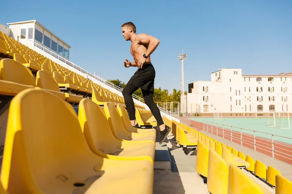 Imagen de deportista sano corriendo por los asientos del estadio mientras hace — Foto de Stock