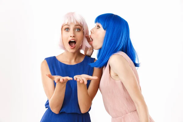 Retrato de dos mujeres sorprendidas con pelucas azules y rosadas hablando secretos en la oreja mientras sostiene el espacio de copia — Foto de Stock