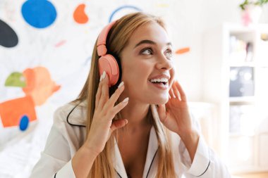 Evde pijama giymiş, yatakta müzik dinleyen tatlı bir kız.