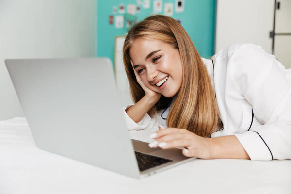 Girl in pajama at home on bed using laptop computer.