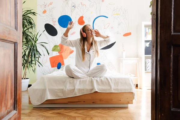 Jolie fille en pyjama à la maison sur le lit écouter de la musique — Photo
