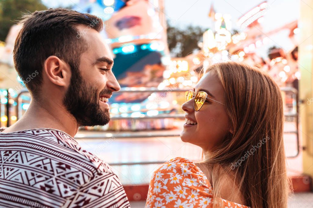 Positive loving couple walking outdoors in amusement park.