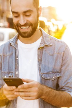 Gülümseyen yakışıklı genç adam cep telefonu kullanıyor.
