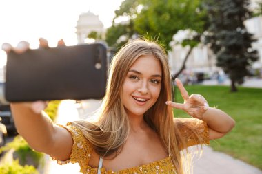 Güzel gülümseyen genç sarışın kız selfie çekiyor.