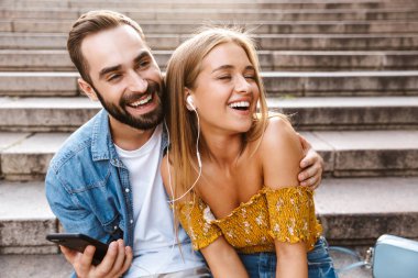 Gülümseyen genç çift merdivenlerde birlikte oturuyor.