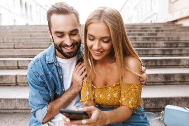 Gülümseyen genç çift merdivenlerde birlikte oturuyor.