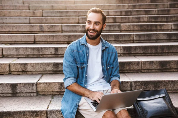 Guapo joven feliz usando ordenador portátil — Foto de Stock