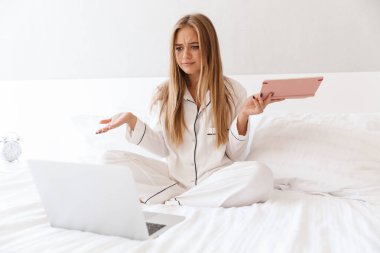 Kafası karışmış genç bir kadının elinde defterle dizüstü bilgisayara bakarken fotoğrafı.