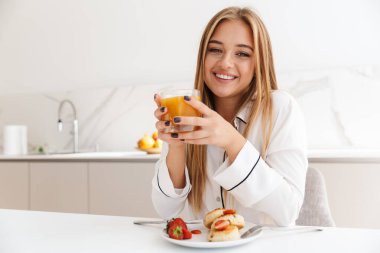 Güzel sarışın bir kadının kahvaltı yaparken ve gülümserken fotoğrafı.