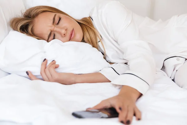 Foto de mujer soñolienta disgustada apagando la alarma en el teléfono celular —  Fotos de Stock