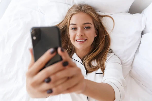 Foto de mujer alegre tomando foto selfie en el teléfono celular mientras está mintiendo —  Fotos de Stock