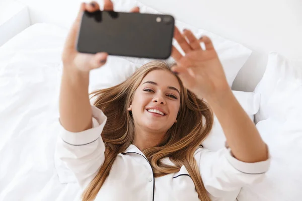 Foto de mujer alegre haciendo foto selfie en el teléfono celular mientras está mintiendo —  Fotos de Stock