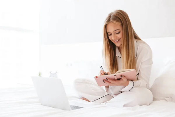 Photo of blonde smiling woman make notes and using laptop — Stock Photo, Image