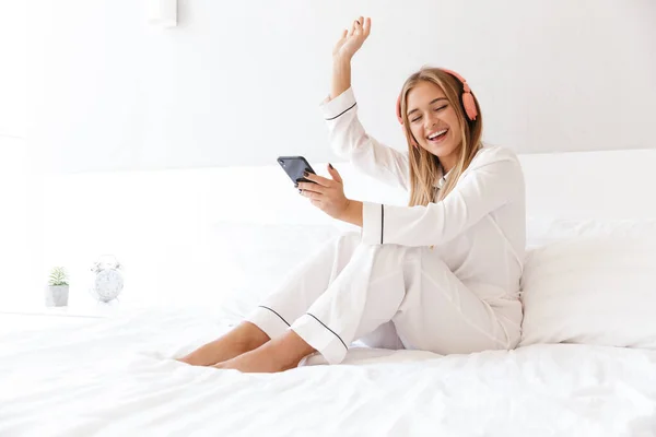 Foto de una mujer sonriente escuchando música con teléfono celular y auriculares —  Fotos de Stock