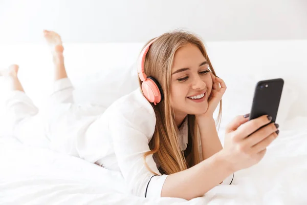 Foto di giovane donna compiaciuta che ascolta musica sdraiata sul letto — Foto Stock