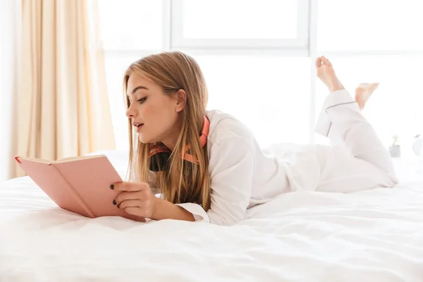 Zdjęcie młodej białej kobiety robiącej notatki leżącej na łóżku — Zdjęcie stockowe