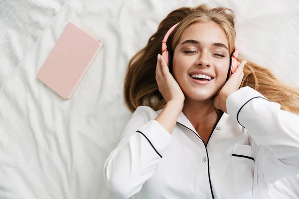 Image de jeune fille heureuse dans les écouteurs souriant tout en étant couché en b — Photo