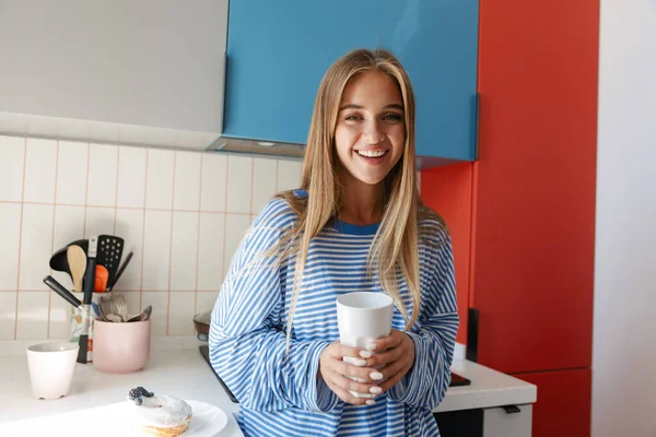 Image of satisfied young girl smiling and drinking tea in kitche — ストック写真