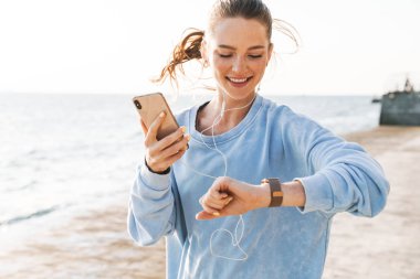 Kumsalda koşan bir kadın saatine bakıyor..