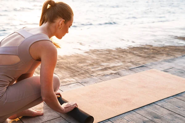 Kvinna utomhus på stranden med fitness matta. — Stockfoto