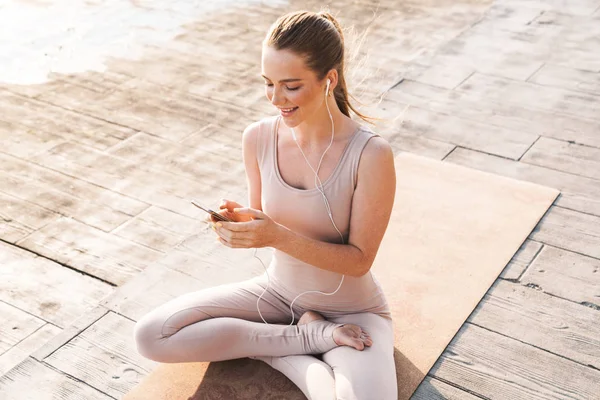 Sportovní žena venku na pláži pomocí mobilního telefonu — Stock fotografie