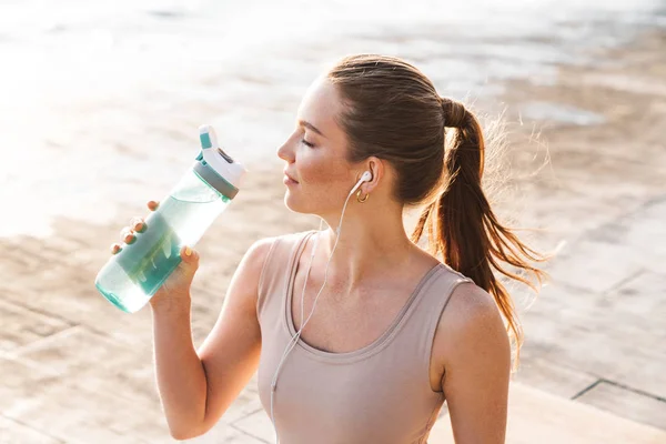 Sport kvinna utomhus på stranden dricksvatten — Stockfoto