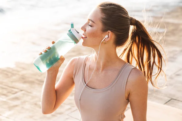 Sport kvinna utomhus på stranden dricksvatten — Stockfoto