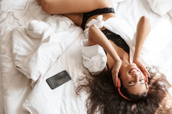 스마트폰을 들고 침대에 누워 헤드폰을 끼고 있는 여성의 모습 — 스톡 사진