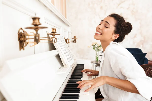 Senhora de camisa branca tocar piano dentro de casa enquanto canta . — Fotografia de Stock