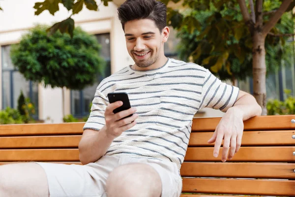 Kép a boldog sörte ember segítségével okostelefon és mosolygós ülés közben — Stock Fotó