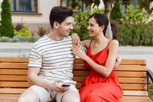 Bild eines glücklich lächelnden Paares, das Handy benutzt und sich im Sitzen umarmt — Stockfoto