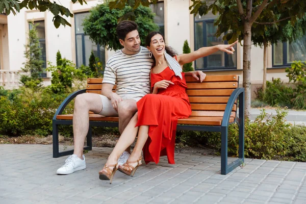 Immagine di una coppia felice e sorridente che punta il dito e si abbraccia seduta — Foto Stock