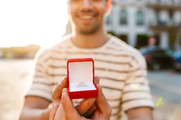 Image of cheerful masculine man smiling and holding gift box with ring — Stockfoto