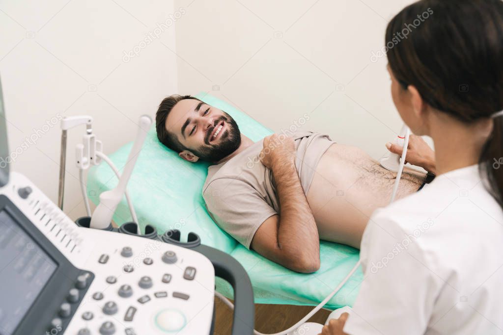Image of smiling man getting abdominal ultrasound scan by female