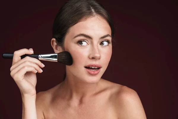 Imagen de una joven mujer semidesnuda mirando a un lado y usando un cepillo de maquillaje —  Fotos de Stock
