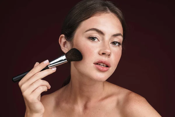 Bild einer halbnackten Frau, die in die Kamera schaut und Make-up-Pinsel benutzt — Stockfoto