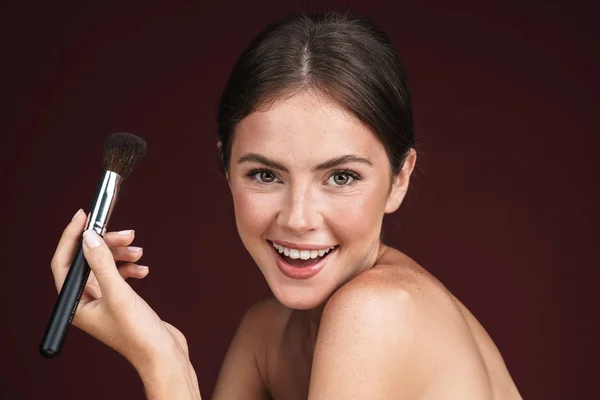 Imagen de la alegre mujer semidesnuda sosteniendo el cepillo de maquillaje —  Fotos de Stock