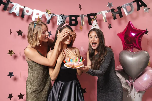 Friends holding cake covering eyes of birthday girl. — ストック写真