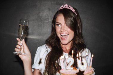 Elinde pasta ve bir bardak şampanya tutan güzel, heyecanlı bir kadın resmi.