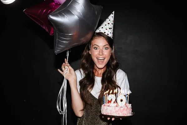 Gülümserken balon ve pasta tutan heyecanlı genç bir kadın resmi — Stok fotoğraf