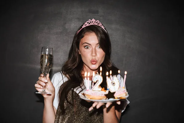 Image of woman holding cakes and glass while making kiss lips