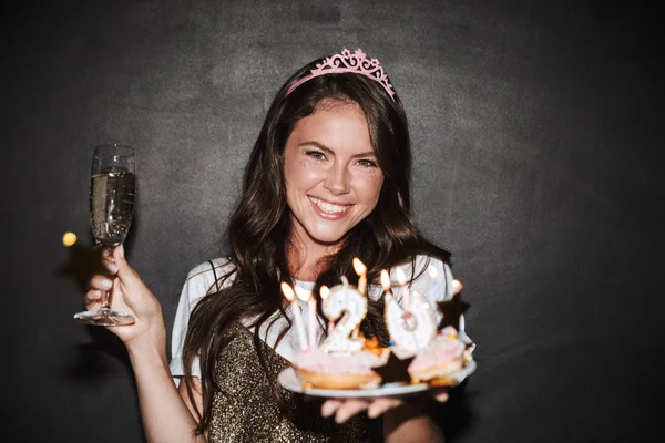 Image of nice excited woman holding cakes and glass of champagne — Stock Photo, Image