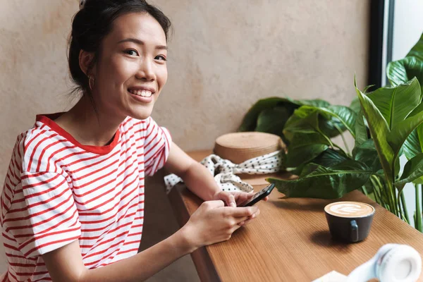 Portret van vrolijke aziatische vrouw glimlachend en met een mobiele telefoon in — Stockfoto
