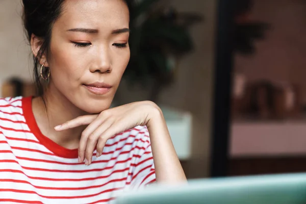 Retrato de mujer asiática seria usando computadora portátil en café en el interior —  Fotos de Stock